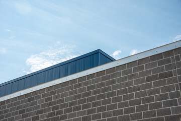 The exterior wall of a commercial building with grey brick, light gray mortar, and silver color flashing or fascia.  There's a deep blue sheet metal siding wall on a high exterior wall above the brick