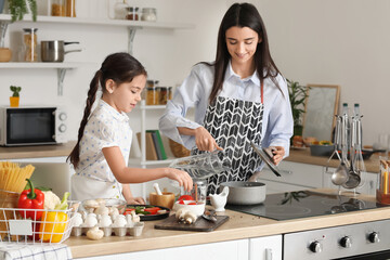 Young mother and daughter cooking together in kitchen at home