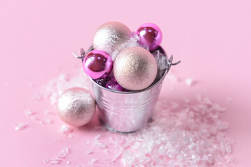 Bucket with Christmas balls and artificial snow on color background