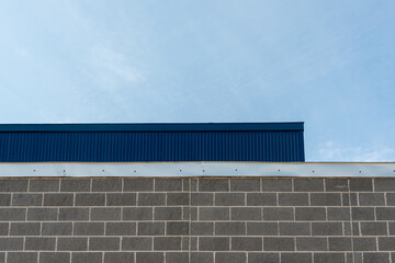 The exterior wall of a commercial building with grey brick, light gray mortar, and silver color flashing or fascia.  There's a deep blue sheet metal siding wall on a high exterior wall above the brick