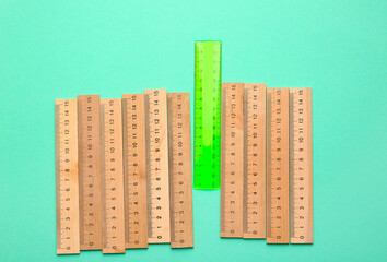 Green ruler among wooden ones on color background. Concept of uniqueness