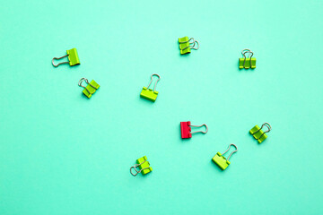 Pink paper clip among green ones on color background. Concept of uniqueness