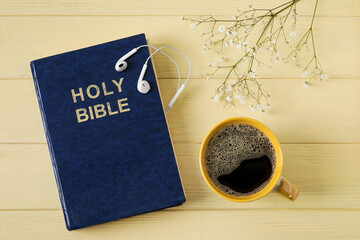 Holy Bible, gypsophila flowers, earphones and cup of coffee on color wooden background