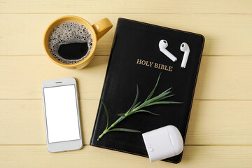 Holy Bible, earphones, mobile phone and cup of coffee on color wooden background
