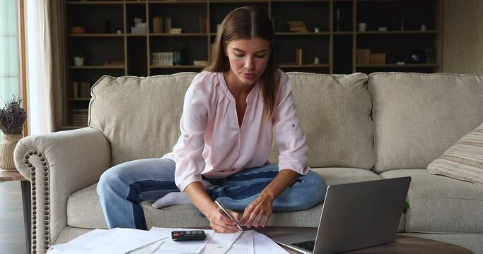 Home economics. Young female working with papers at home office pay utility bills plan budget using laptop. Focused gen z woman manage receipts invoices count and provide student loan payment online