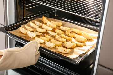 Woman taking baking tray with fresh potato out of oven