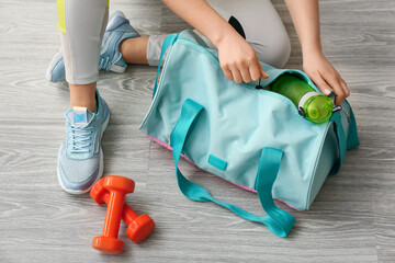 Woman in sport shoes preparing bag for training on light wooden floor