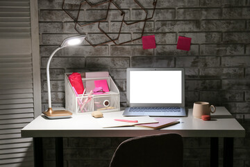 Stylish workplace with modern laptop and lamp in evening