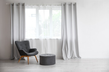 Modern armchair and pouf near window in room