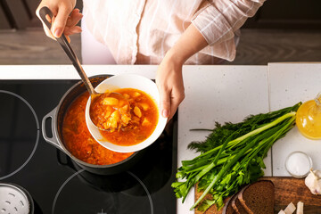 Woman pouring delicious borscht from cooking pot to bowl in kitchen