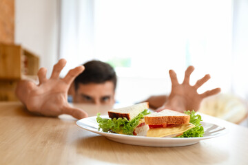 Young man with tasty sandwich at home