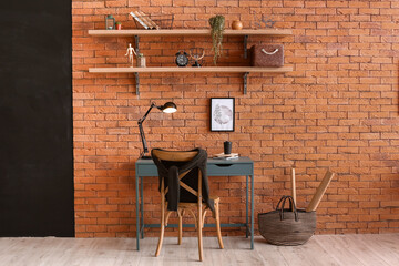 Interior of room with stylish workplace and shelves with different decor on brick wall