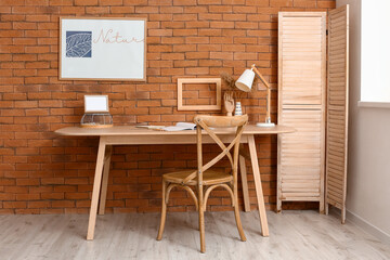 Interior of room with comfortable workplace and painting with word NATURE on brick wall