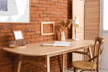 Comfortable workplace with stationery supplies, blank photo frame, lamp and decor on table