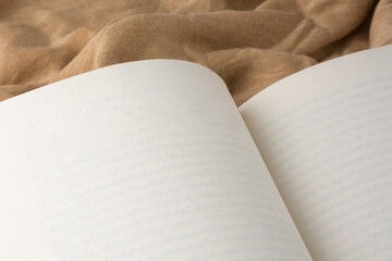 opened blank book on a light brown fabric background, closeup paperback mockup template with copy space