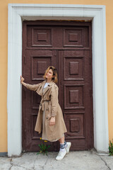 Young millennial woman with wild hair dressed in an autumn coat posing near the door of an old building.