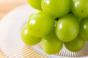 Bunch of Shine-Muscat grapes on a plate set against a wooden background.