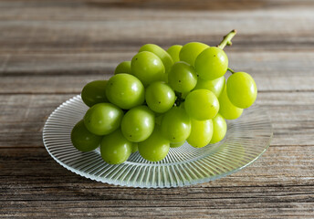 Shine Muscat grapes on a glass plate set against a wooden background.