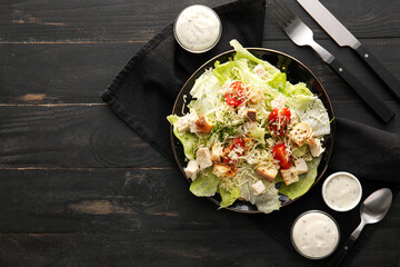 Plate of tasty Caesar salad bowls with sauce on black wooden background