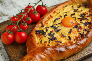 Wooden board with tasty Ajarian khachapuri and tomatoes on grunge background, closeup