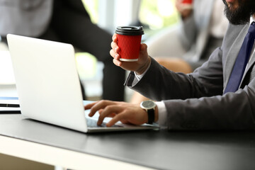 Man drinking coffee while working on laptop in office, closeup