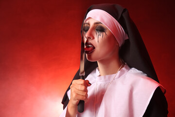 Woman dressed for Halloween as nun with knife on color background