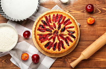 Board with tasty plum pie on wooden background