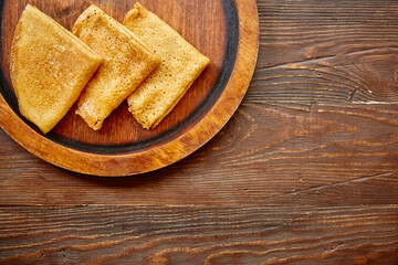 Delicious homemade pancakes on a handmade wooden plate on a textured antique countertop. The concept of a simple natural home food.