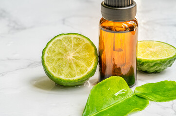 Beautiful packshot of Bergamot essential oil in a small brown glass bottle with fresh bergamot fruit with green leaf on the marble tabletop, wet of water. Blank space on the bottle for branding. - obrazy, fototapety, plakaty
