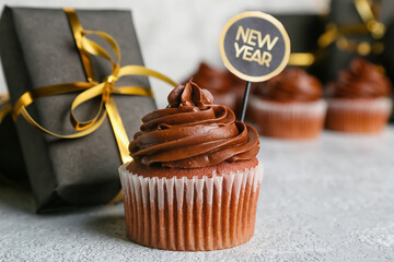 Tasty cupcake for New Year 2022 celebration with gift on grunge background