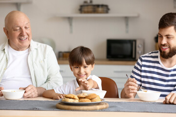 Happy man, his little son and father having breakfast in kitchen