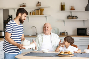 Obraz premium Happy man, his little son and father having breakfast in kitchen