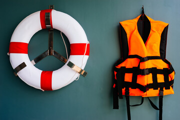 Orange life jacket and white-red life bouy hang on the wall together for keeping a person afloat in water