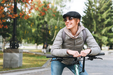 Portrait of fashionable young pretty woman in cap and sunglasses on bicycle on sunny autumn day in...