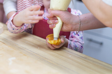 A child learns to fill eclair cakes with cream from a pastry bag