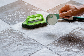Close up a human hand pours detergent onto the wet tile floor to clean it.