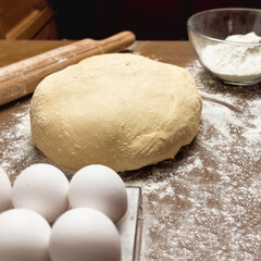 Flour, eggs and dough are placed on the table in the home kitchen.
close-up of dough on dark wooden background. blurred foreground. raw fresh dough for baking in home kitchen

