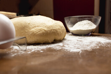 close-up of dough on a dark wooden table background. Flour and eggs and dough components are located side by side. raw fresh dough for baking in home kitchen

