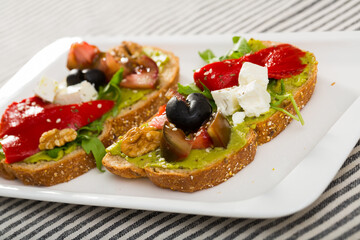 Fototapeta na wymiar Sandwich with avocado, feta cheese, vegetables and walnut at plate..
