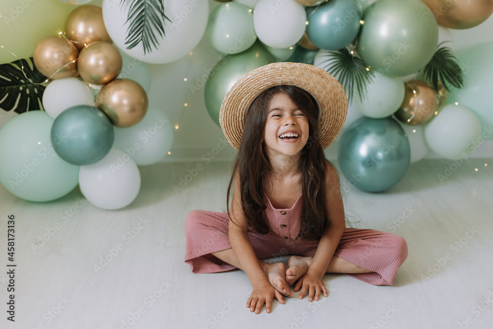 Wall mural beautiful smiling little dark-skinned girl with brown eyes and dark hair in a straw hat and a dusty 