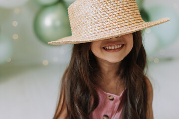 Closeup portrait of a beautiful smiling little dark-skinned girl with brown eyes and dark hair in a straw hat against the background of balloons. Concept of spring summer youth beauty. Beautiful face