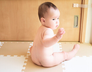 お座りをして裸でおむつをしている赤ちゃんの後ろ姿