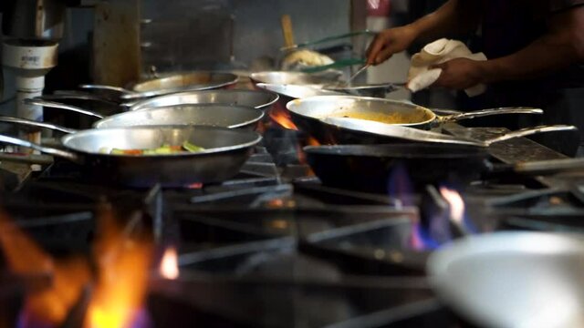 Professional restaurant kitchen staff stir saute various dishes over high heat range top stove with flare ups, cinematic slow motion slider HD