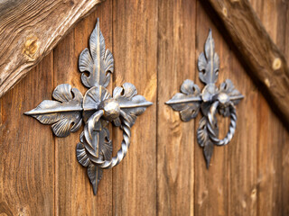 Door handles on a wooden door in the form of forged bronze rings, close-up. Ancient
