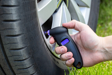 A person measures the pressure in the wheel of a car with a special electronic pressure gauge,...