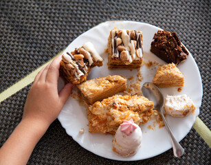 Child's hand holds a cake in a plate, scraps of sweets. Sweet tooth, close-up