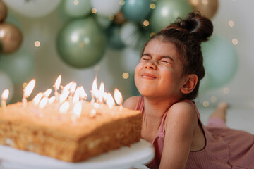 Little dark-skinned girl makes a wish and blows out the candles on the birthday cake. Cute girl...