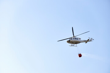 Firefighting helicopter transporting water to extinguish a fire. Hazard concept