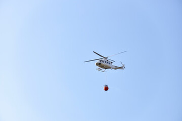 Firefighting helicopter transporting water to extinguish a fire. Hazard concept