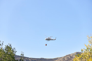 Firefighting helicopter transporting water to extinguish a fire. Hazard concept